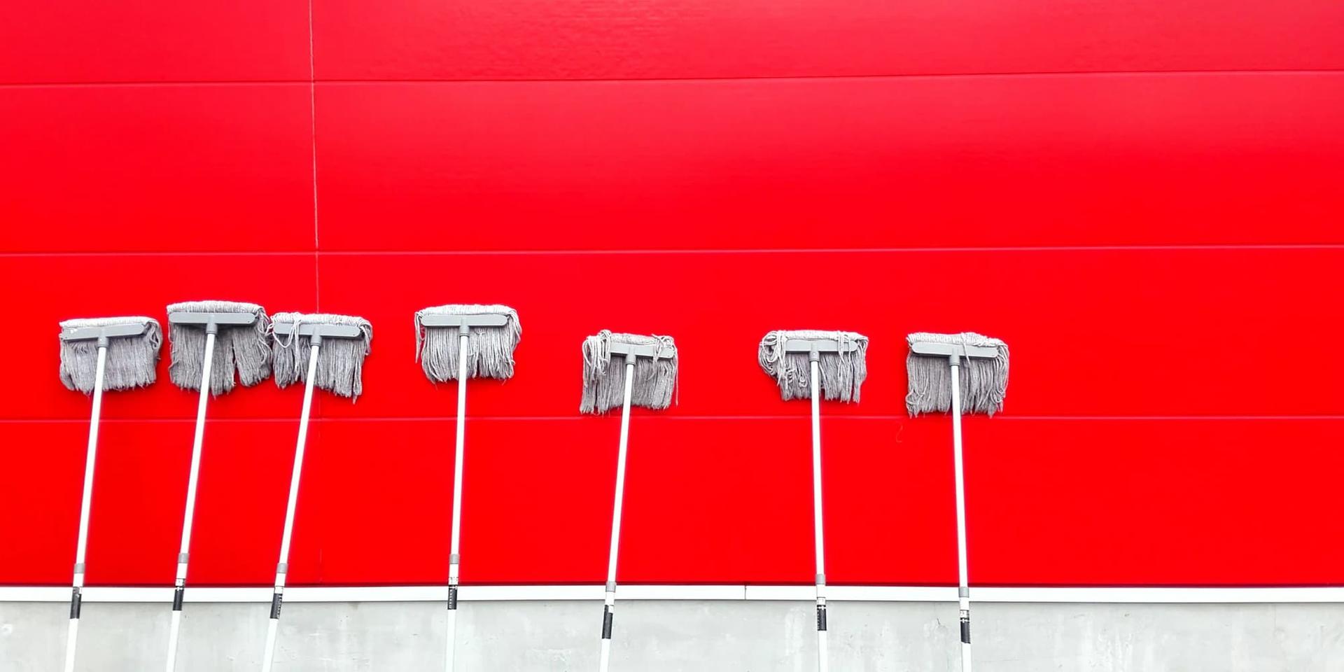 Seven mops leaning against a red wall